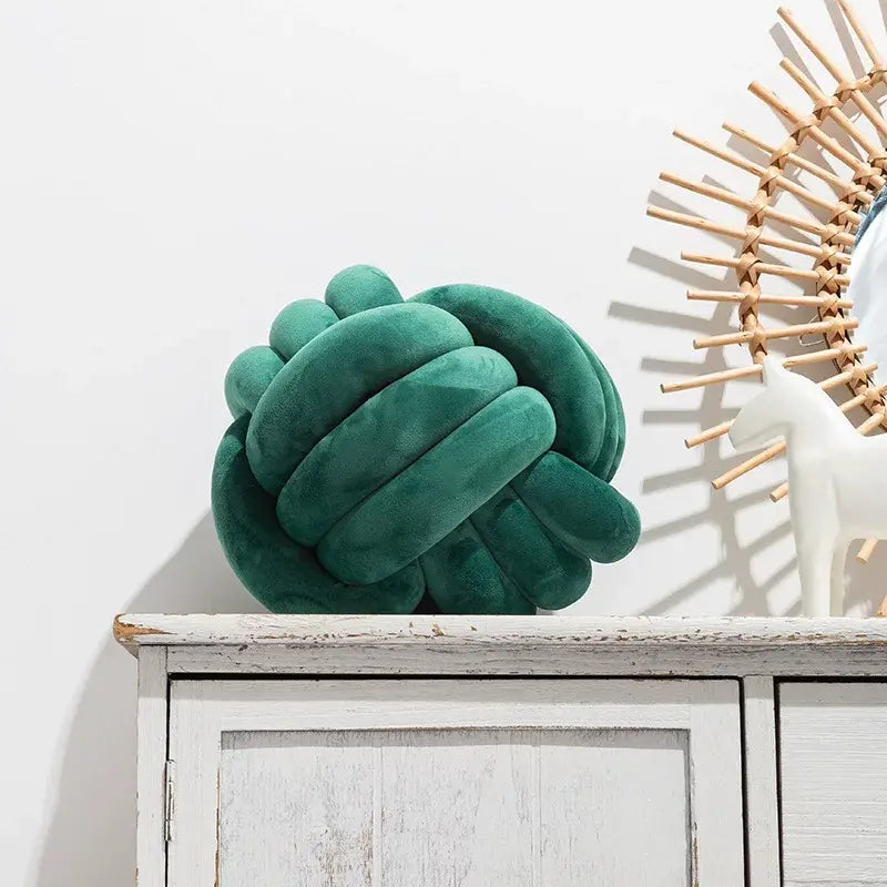 Green knotted pillow on a white cabinet with a decorative mirror in the background